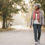An older woman smiling gently during a peaceful morning walk on a tree-lined path.